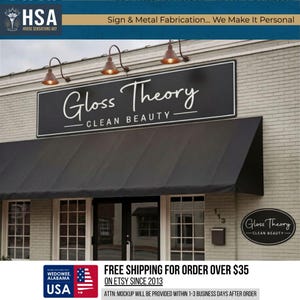May include: Exterior shot of a storefront with a black awning and a sign that reads "Gloss Theory - Clean Beauty." The sign is black with white lettering. The building is brick with three hanging lights above the sign. A smaller sign is on the right.