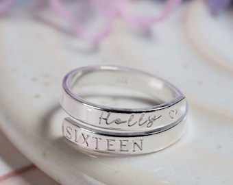 May include: Silver ring with the name "Holly" and the word "Sixteen" engraved on it. The ring is on a white surface with a silver star.