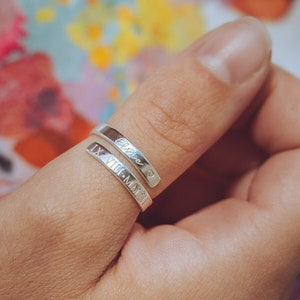 May include: A silver ring with the words "IX.VIII.MMXI" and "Forever" engraved on it. The ring is worn on a person's thumb.