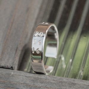 May include: A silver ring with the numbers 20, 06, and 16 engraved on it.