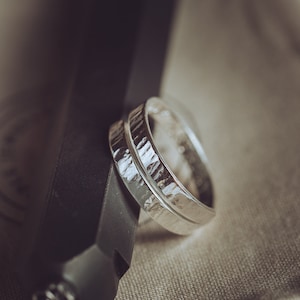 May include: Two silver wedding bands with a textured finish. The bands are stacked on top of each other.