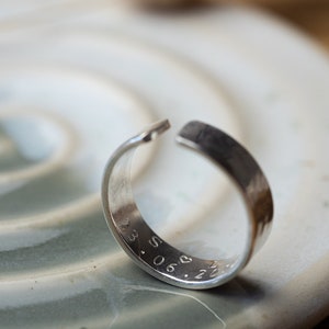 May include: A silver ring with a hammered finish and engraved with the date "23.06.21" and a heart symbol.