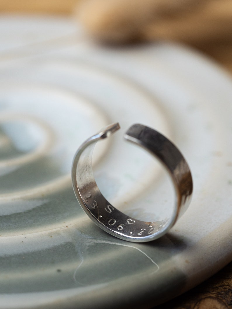 May include: A silver ring with a hammered finish and engraved with the date "23.06.21" and a heart symbol.