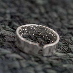 May include: Silver ring with the inscription "Love you more. I win." on the band.