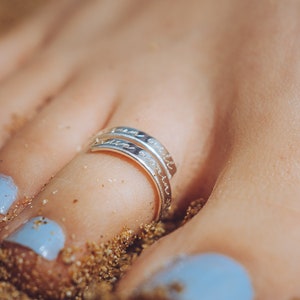 May include: A silver toe ring with the words "sun and salt" engraved on it. The ring is worn on a foot with blue nail polish.