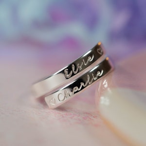 May include: Two silver rings with the names "Elsie" and "Charlie" engraved on them. The rings are intertwined and the name "Charlie" has a small heart symbol before it.