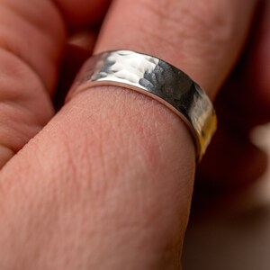 May include: A silver hammered band ring worn on a finger.