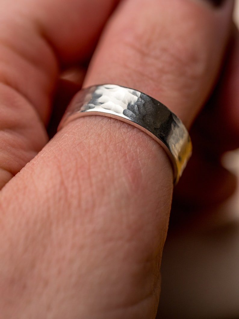 May include: A silver hammered band ring worn on a finger.