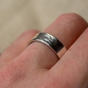 May include: A silver hammered band ring worn on a finger.