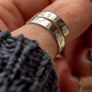 May include: A silver wrap ring featuring an engraved leaf pattern around the band. The ring is displayed on a finger, highlighting the detailed design and polished finish. The ring's design is a nature-inspired jewellery piece.