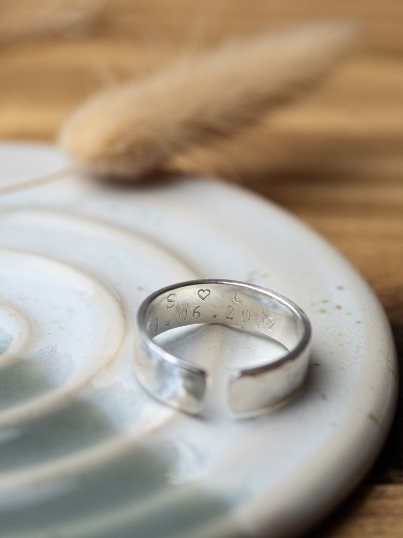 May include: A silver band ring with a heart and the inscription "S &hearts; I 3.06.2012" engraved on the inside.