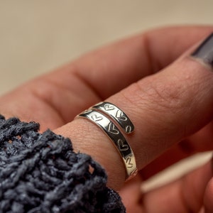 May include: A silver ring with a heart design wrapped around a finger.