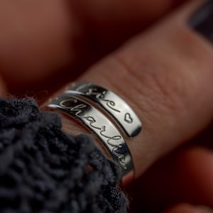 May include: Two silver rings with the words "Charlie" and "Love" engraved on them. The rings are worn on a finger.