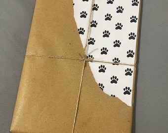 May include: A brown paper package wrapped with twine and tied in a bow. The package is decorated with a white paper with a black paw print pattern.