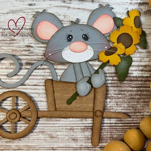May include: A gray mouse with a curled tail holding a bouquet of yellow sunflowers in a wooden wheelbarrow. The mouse has pink ears and a pink nose. The wheelbarrow has a brown wooden body and a brown wooden wheel.