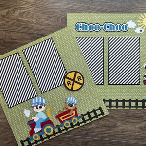 May include: Two scrapbook pages with a train theme. One page features a train with a conductor and a bear, the other has the text "Choo-Choo" and a sun. Both pages have black and white striped elements and a railroad crossing sign.