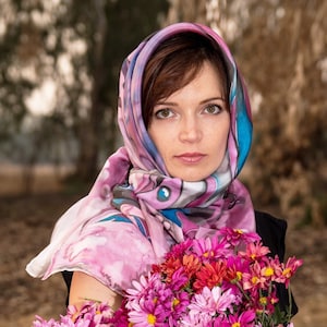 May include: A woman wearing a pink and blue patterned silk scarf holds a bouquet of pink and red chrysanthemums.