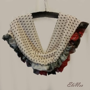 以下が含まれることがあります： 黒のドット柄の白いスカーフで、フリルが付いています。フリルは緑、青、赤の色合いです。