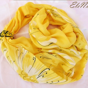 May include: A yellow scarf with a floral pattern and black beads. The scarf is folded and tied with the beads.