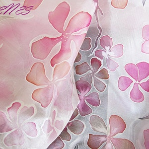 May include: A white silk scarf with a pink floral pattern. The flowers are painted in shades of pink and orange.