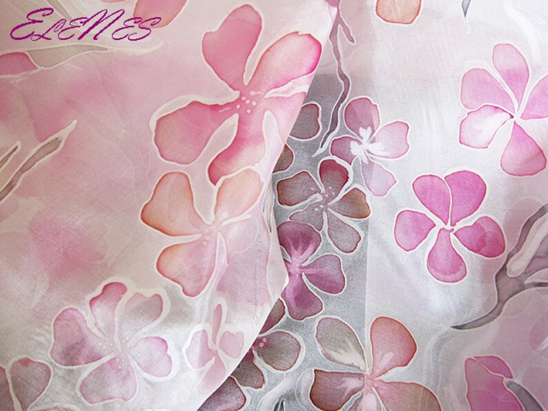 May include: A white silk scarf with a pink floral pattern. The flowers are painted in shades of pink and orange.