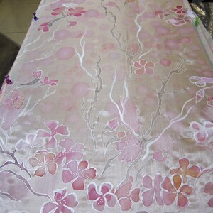 May include: A white silk fabric with a delicate pink floral pattern. The fabric has a subtle sheen and is perfect for crafting or sewing projects.