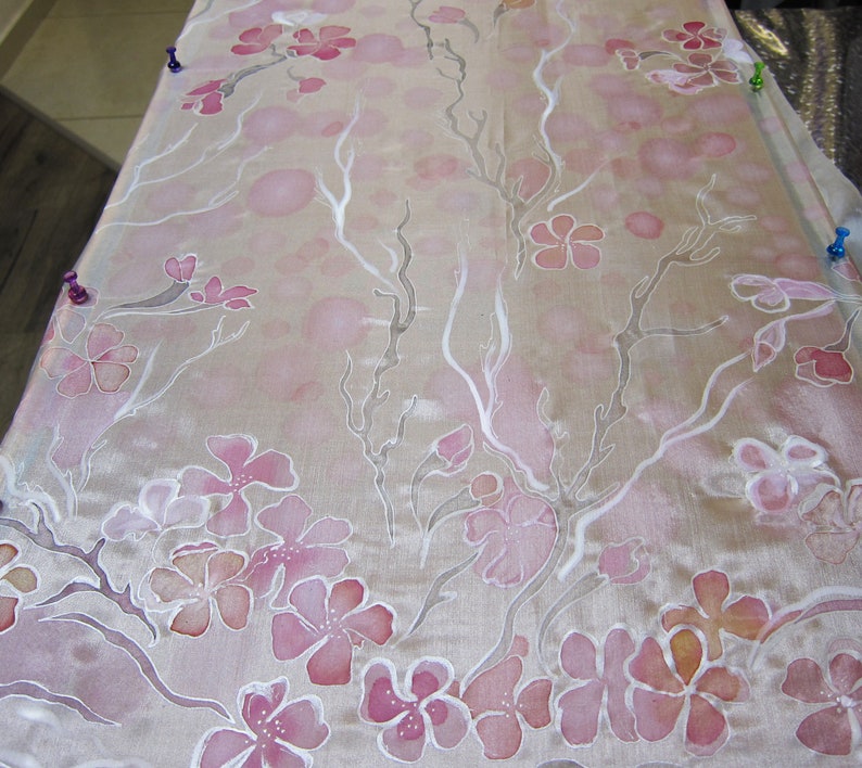 May include: A white silk fabric with a delicate pink floral pattern. The fabric has a subtle sheen and is perfect for crafting or sewing projects.