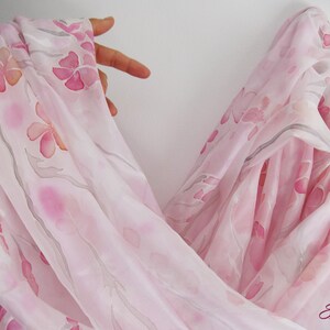 May include: A sheer pink scarf with a delicate floral pattern. The scarf is made of silk and has a soft, flowing drape.