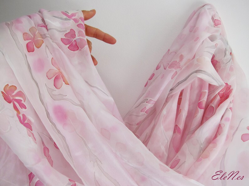 May include: A sheer pink scarf with a delicate floral pattern. The scarf is made of silk and has a soft, flowing drape.
