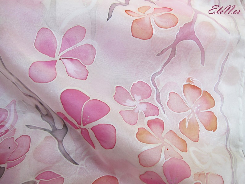 May include: A pink silk scarf with a delicate floral pattern of pink and orange flowers. The flowers are painted in a watercolor style and have a soft, ethereal look. The scarf is made of a lightweight, flowing fabric that is perfect for spring and summer.