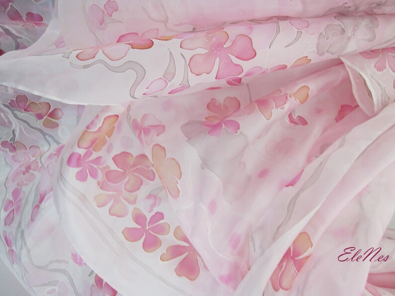 May include: A white silk scarf with a delicate pink floral pattern. The scarf is made of soft, flowing silk and features a subtle ombre effect.