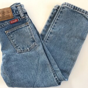 May include: A pair of light blue denim jeans with a brown leather patch that says "Wrangler" on the back pocket.