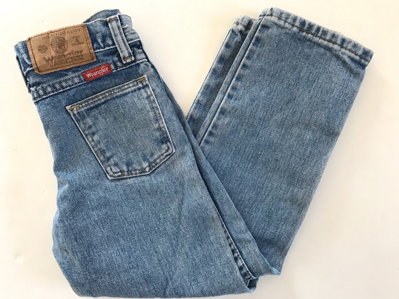 May include: A pair of light blue denim jeans with a brown leather patch that says "Wrangler" on the back pocket.