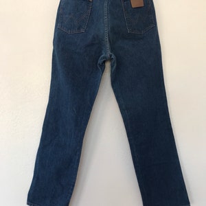 May include: A pair of dark blue denim jeans with a brown leather patch on the back pocket that says "Wrangler".