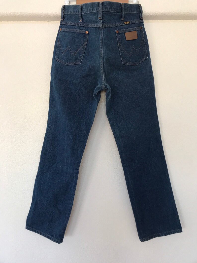 May include: A pair of dark blue denim jeans with a brown leather patch on the back pocket that says "Wrangler".