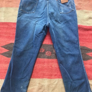 May include: A pair of blue denim jeans with a brown leather patch on the back pocket that says "Wrangler".