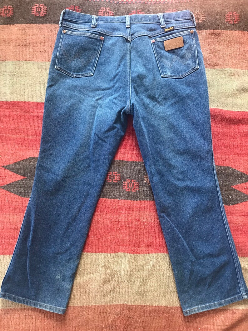 May include: A pair of blue denim jeans with a brown leather patch on the back pocket that says "Wrangler".