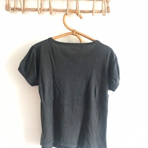 May include: A black short-sleeved t-shirt hanging on a wooden hanger. The t-shirt is plain with no visible graphics or text.