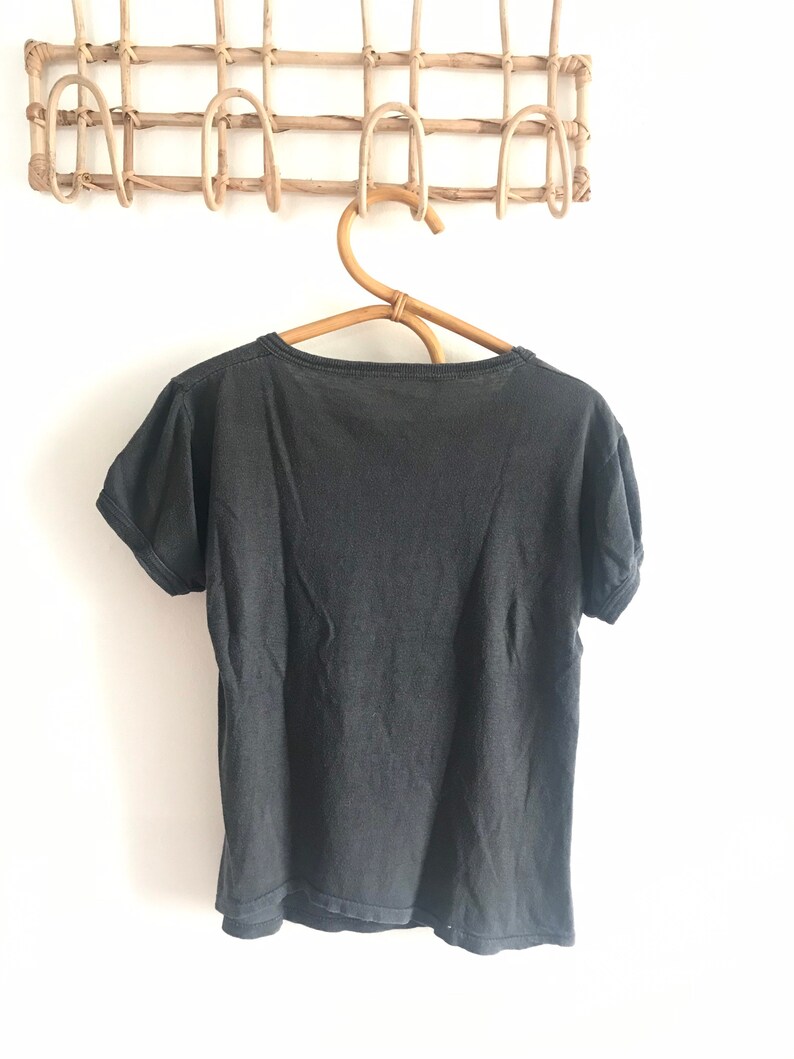 May include: A black short-sleeved t-shirt hanging on a wooden hanger. The t-shirt is plain with no visible graphics or text.