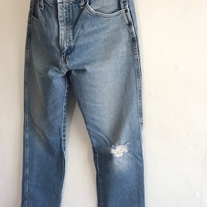 Pu&ograve; includere: Jeans in denim blu chiaro con un ginocchio consumato e una sola tasca posteriore. I jeans hanno una gamba dritta e una vestibilit&agrave; classica.