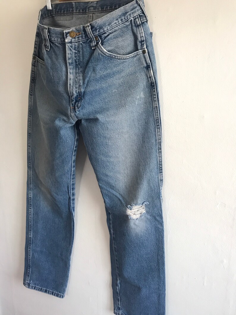Pu&ograve; includere: Jeans in denim blu chiaro con un ginocchio consumato e una sola tasca posteriore. I jeans hanno una gamba dritta e una vestibilit&agrave; classica.