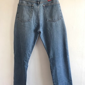 Pu&ograve; includere: Un paio di jeans in denim blu chiaro con un'etichetta Wrangler in pelle marrone sulla tasca posteriore.