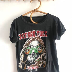 May include: Black t-shirt with a graphic of a man wearing binoculars and the text "Jethro Tull - Stormwatch Tour '80".
