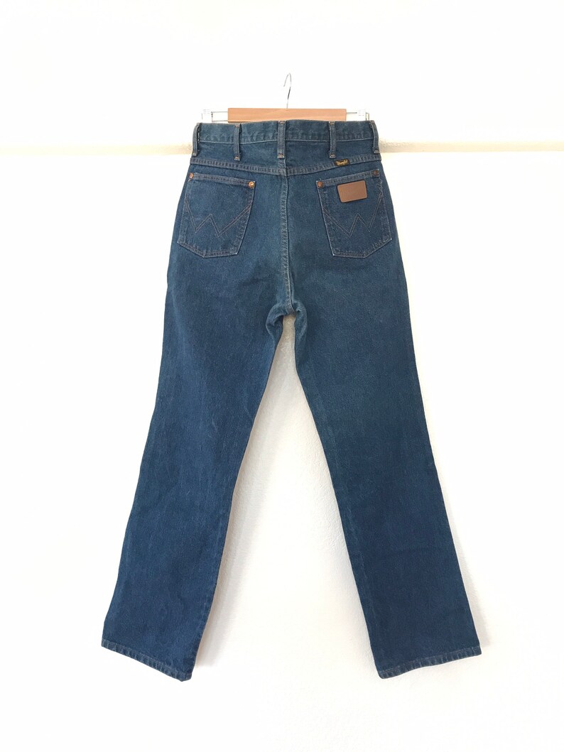 May include: A pair of dark blue denim jeans with a brown leather patch on the back pocket that says "Wrangler".