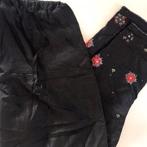 May include: Two pairs of black pants. One pair is plain and the other pair has red and blue floral embroidery.