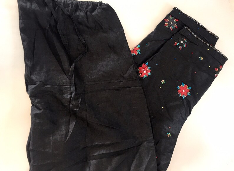 May include: Two pairs of black pants. One pair is plain and the other pair has red and blue floral embroidery.