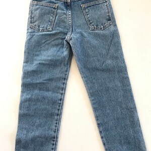 May include: A pair of light blue denim jeans with a brown leather patch on the back pocket that says "Wrangler" in white text.