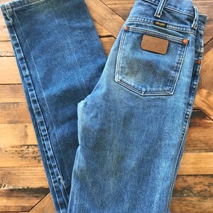 May include: A pair of blue denim jeans with a brown leather Wrangler patch on the back pocket.