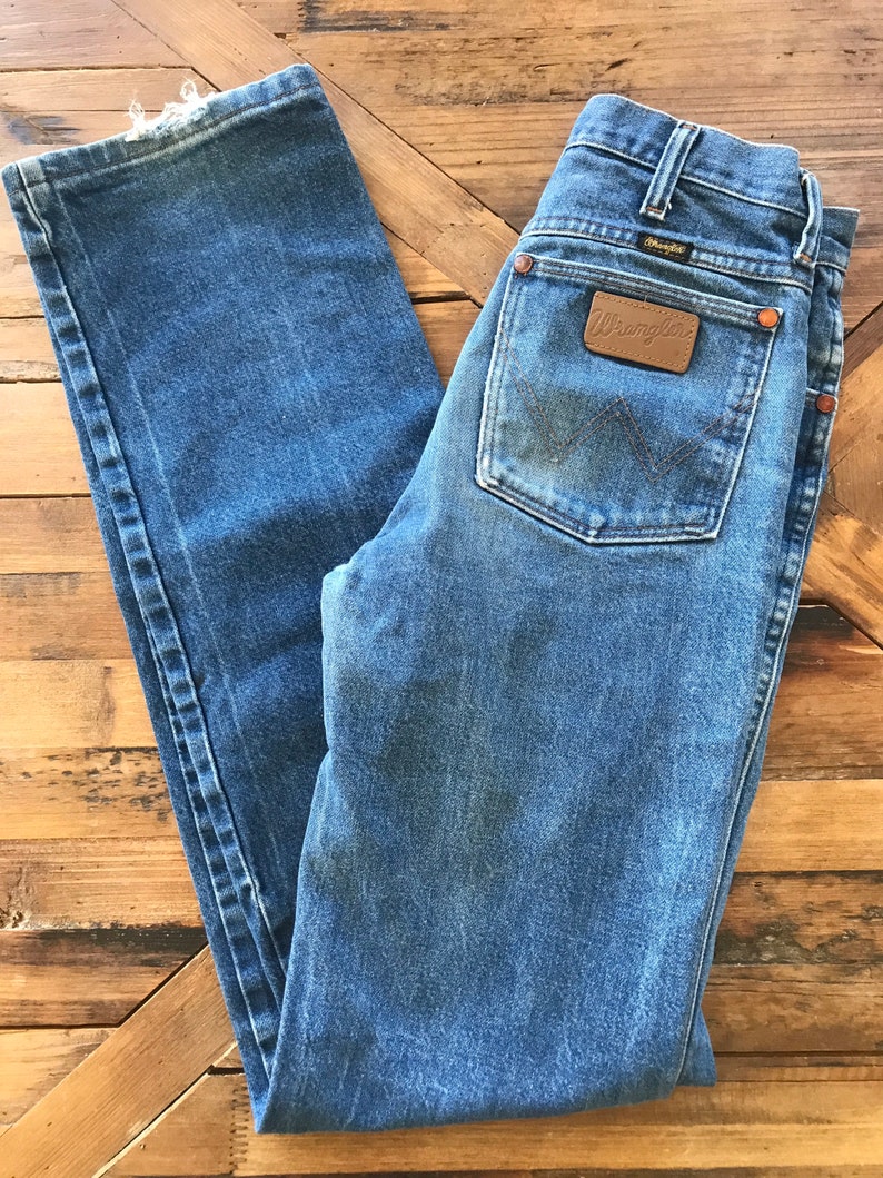 May include: A pair of blue denim jeans with a brown leather Wrangler patch on the back pocket.