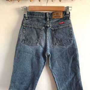May include: A pair of light blue denim shorts with a frayed hem. The shorts have a brown leather patch on the back with the text "Premium Quality Wrangler" in white.